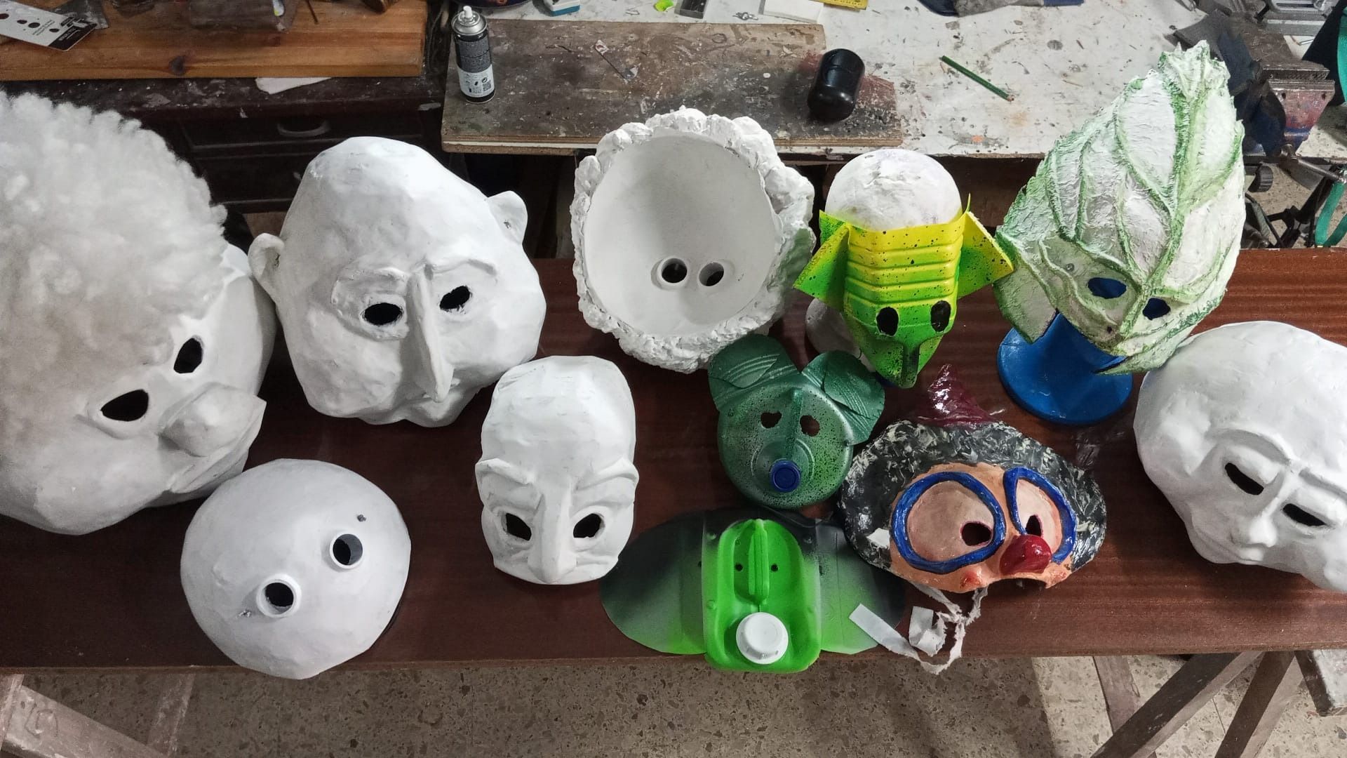 Una colección de máscaras hechas a mano sobre una mesa de madera, que varían en estilo desde lo simple a lo elaborado, con varios colores.